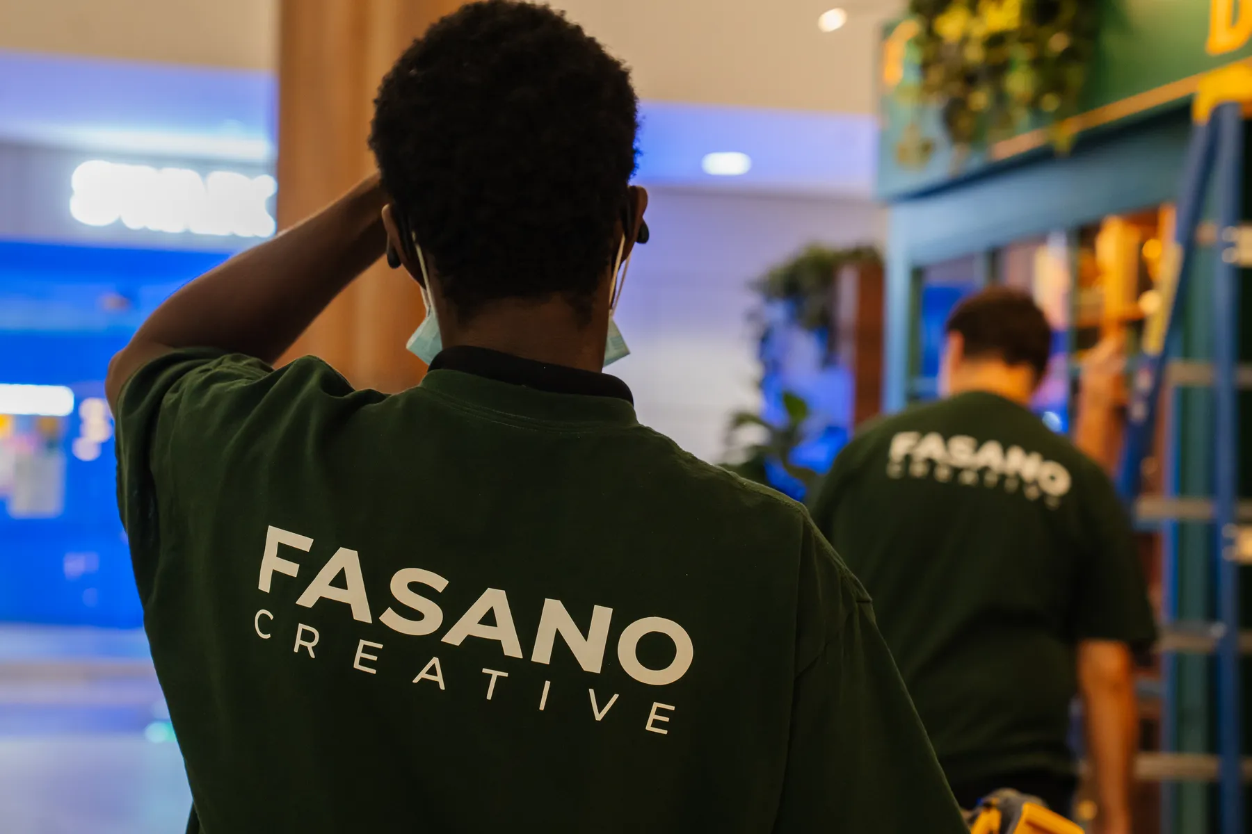 Two Fasano Creative crew members in branded shirts, seen from behind, installing The Book Corner