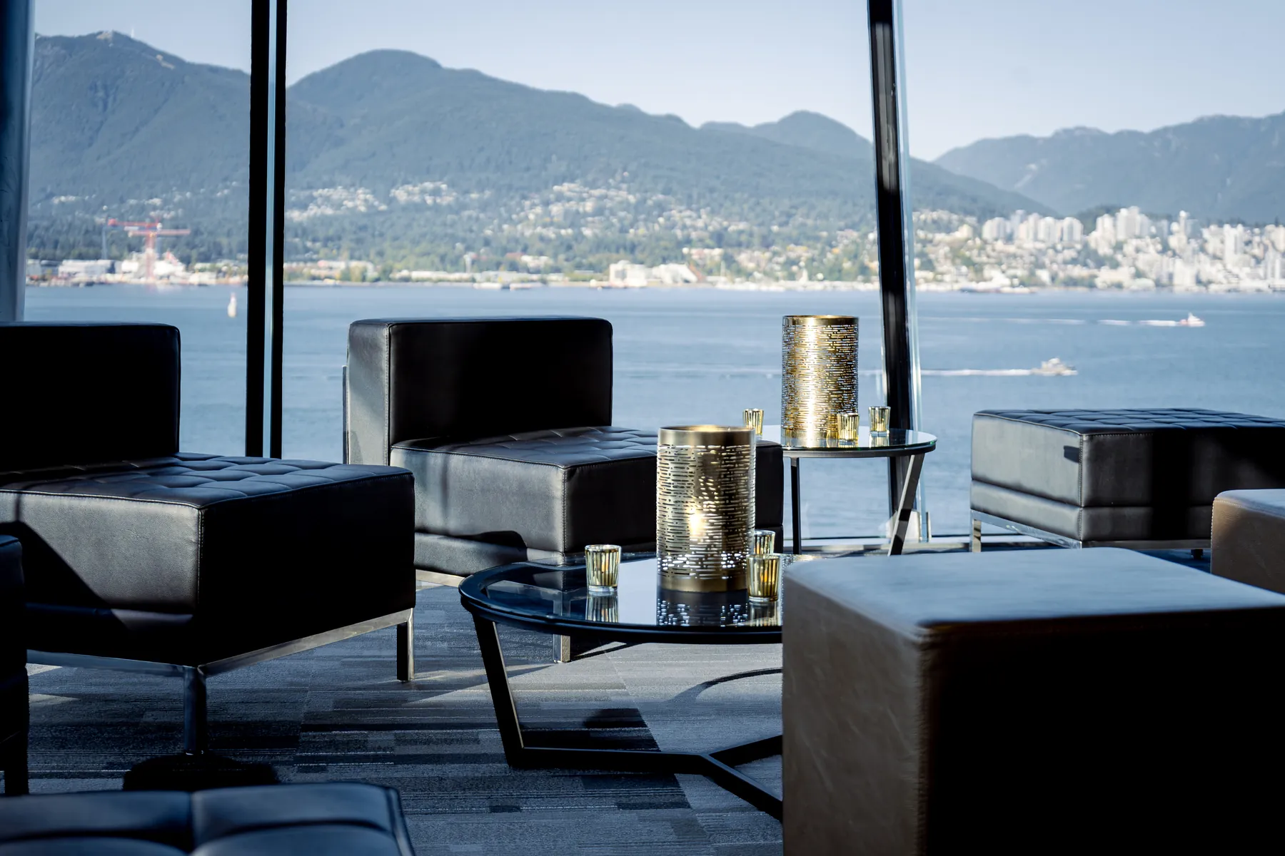 Black leather lounge seating with gold lanterns in front of floor-to-ceiling windows over Vancouver Harbour and the North Shore mountains